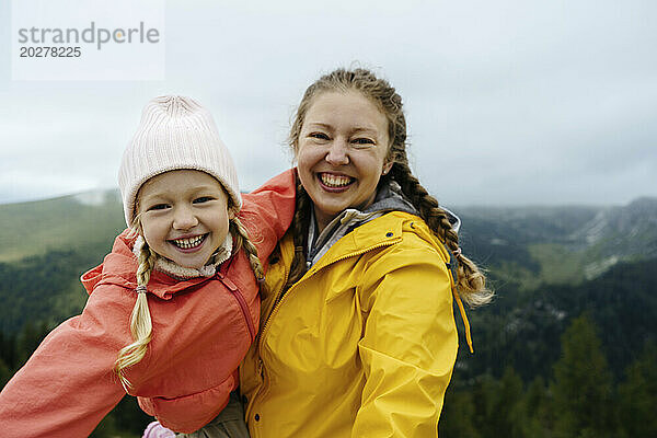 Cheerful mother carrying daughter on mountain
