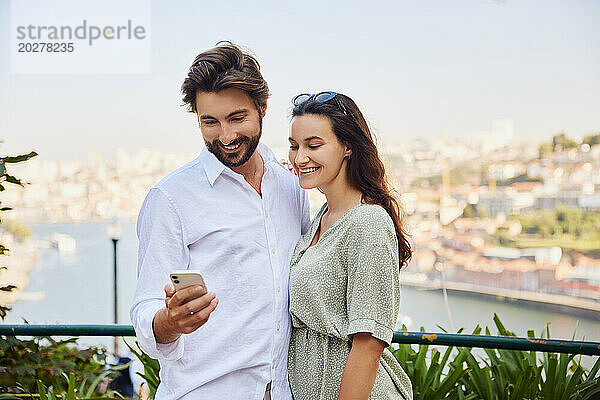 Glückliches junges Paar  das an einem sonnigen Tag sein Smartphone benutzt