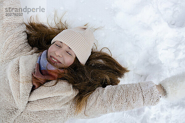 Lächelnde junge Frau  die auf Schnee liegt
