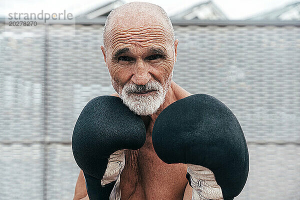 Selbstbewusster älterer Mann ohne Hemd  der mit Boxhandschuhen übt