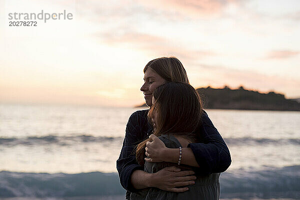 Freunde umarmen sich im Urlaub am Strand bei Sonnenuntergang