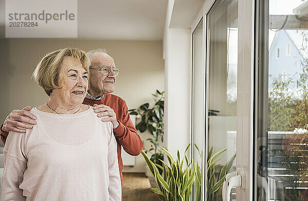 Glücklicher älterer Mann und ältere Frau  die zu Hause durch das Fenster schauen