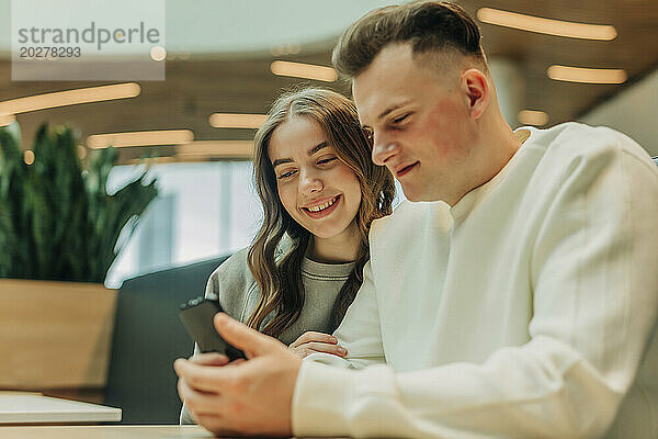 Mann benutzt Smartphone und sitzt mit Freundin im Einkaufszentrum
