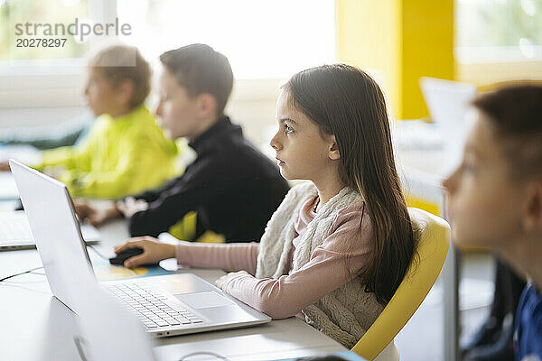 Engagiertes Mädchen benutzt Laptop am Schreibtisch und lernt im Klassenzimmer Computerprogrammierung