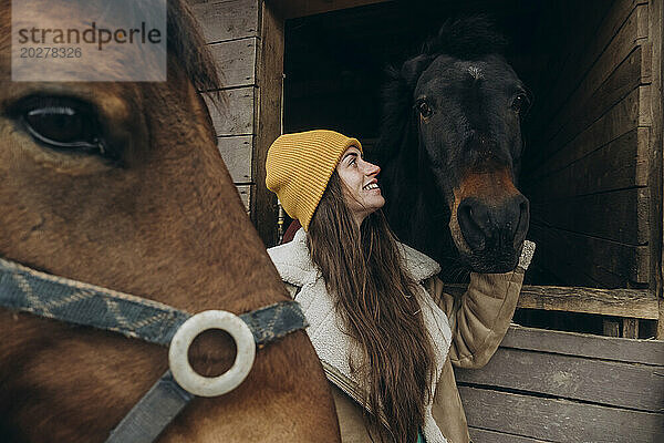Lächelnde Frau streichelt Pferde im Stall auf dem Bauernhof