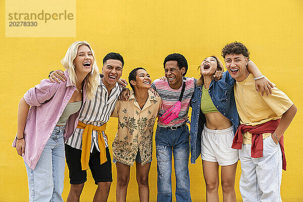 Sorglose Freunde in farbenfroher Kleidung stehen mit den Armen um die gelbe Wand