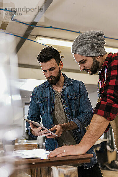 Junge Tischler teilen sich in der Werkstatt einen Tablet-PC