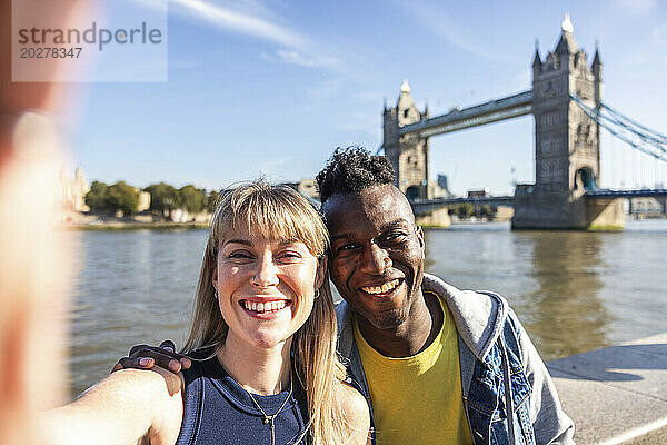 Happy multiracial friends taking selfie with Tower bridge in background