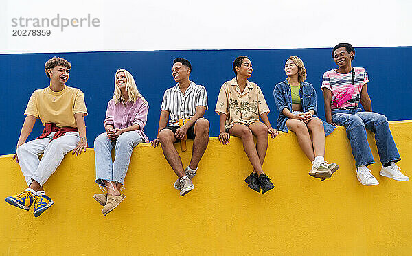 Fröhliche Freunde mit bunter Kleidung sitzen zusammen an einer gelben Wand
