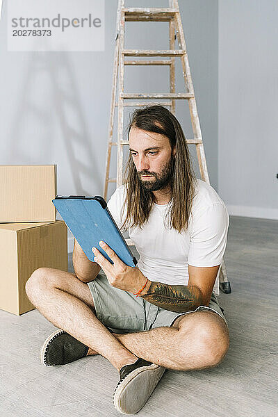 Mann sitzt auf dem Boden und benutzt Tablet-PC im neuen Zuhause