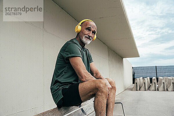 Älterer Mann  der Musik über kabellose Kopfhörer hört und auf einer Bank sitzt