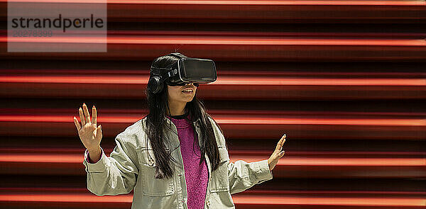 Glückliche junge Frau gestikuliert mit Virtual-Reality-Simulatoren