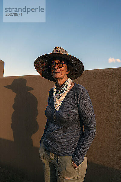 USA  New Mexico  Santa Fe  Porträt einer Frau mit Strohhut  die vor einer Lehmwand in der High Desert steht