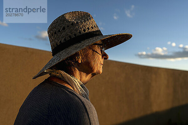 USA  New Mexico  Santa Fe  Frau mit Strohhut steht vor einer Lehmwand in der High Desert