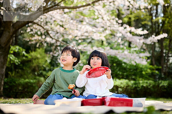 Zwei Kinder sitzen auf einer Decke mit einem roten Teller