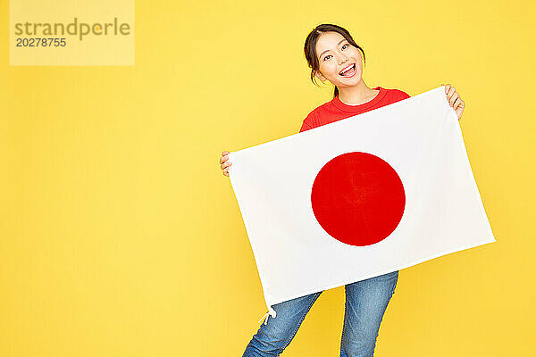 Eine Frau hält eine japanische Flagge auf gelbem Hintergrund