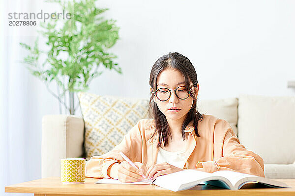 Eine Frau mit Brille sitzt mit einem Buch und einem Stift an einem Tisch