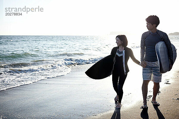 Ein Mann und eine Frau gehen mit Surfbrettern am Strand spazieren