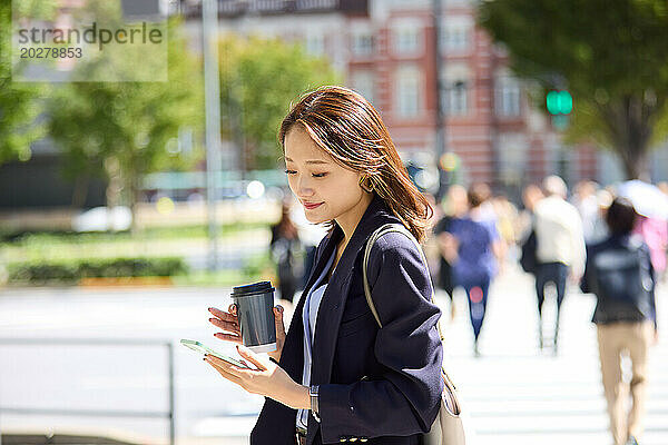 Asiatische Frau benutzt Smartphone  während sie auf der Straße geht