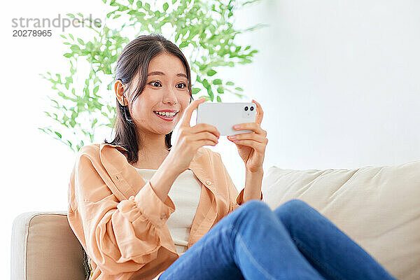 Asiatische Frau sitzt auf der Couch und macht ein Selfie mit ihrem Handy