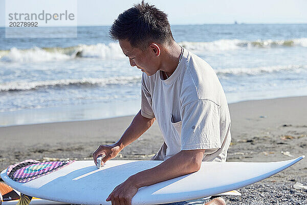 Ein Mann sitzt mit einem Surfbrett am Strand
