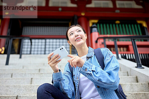 Asiatische Frau sitzt auf Stufen mit Telefon in der Hand