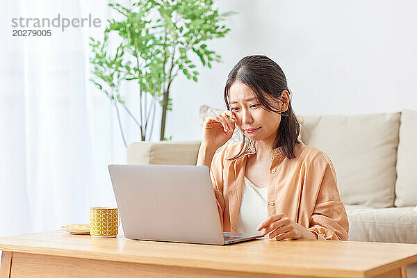 Asiatische Frau sitzt mit Laptop auf der Couch