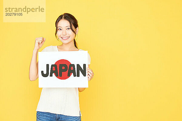 Japanerin hält Schild mit japanischem Text auf gelbem Hintergrund hoch