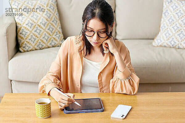 Eine Frau mit Brille sitzt an einem Tisch mit einem Tablet und einer Tasse Kaffee