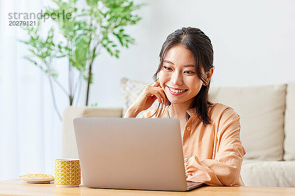 Asiatische Frau benutzt Laptop im Wohnzimmer