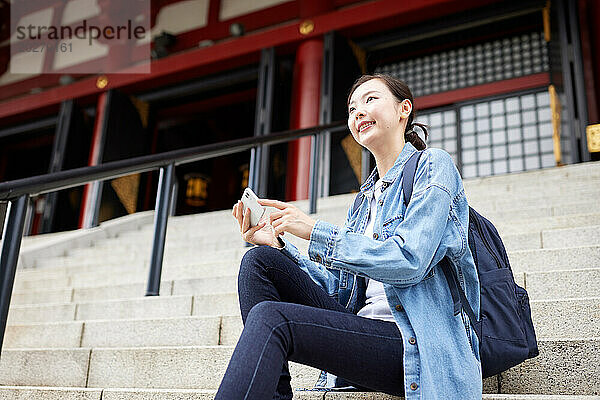 Asiatische Frau sitzt mit ihrem Telefon auf einer Treppe