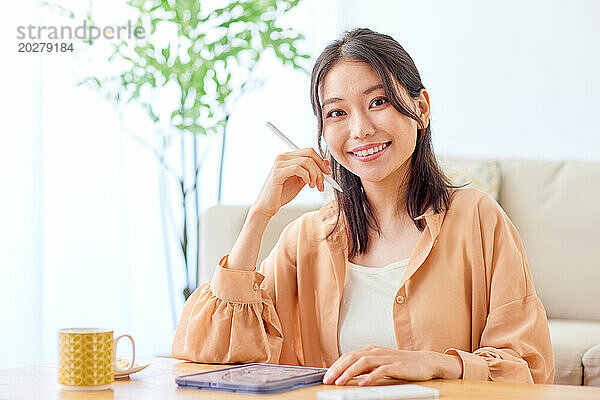 Asiatische Frau sitzt mit Tablet und Kaffee am Tisch