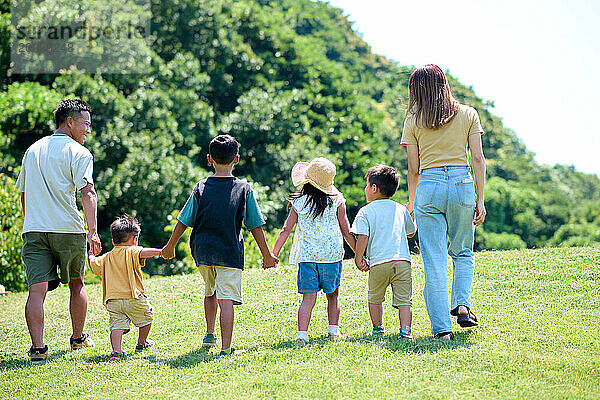 Eine Familie geht Händchen haltend im Gras spazieren