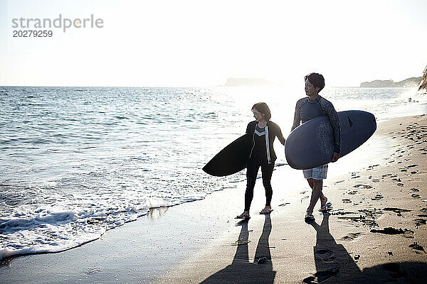 Ein Mann und eine Frau gehen mit Surfbrettern am Strand spazieren