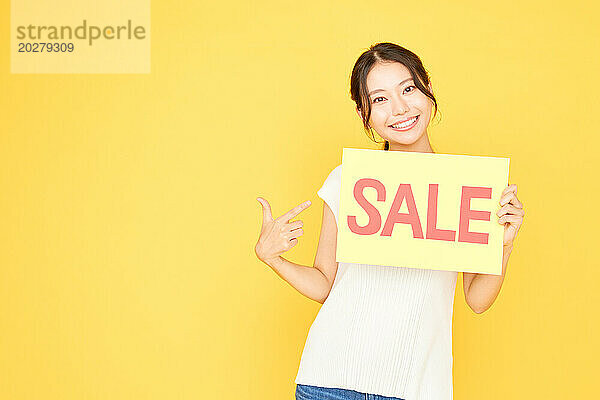 Glückliche asiatische Frau hält ein Verkaufsschild auf gelbem Hintergrund hoch