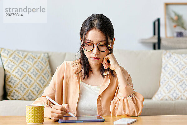 Eine Frau mit Brille sitzt mit Tablet und Stift an einem Tisch