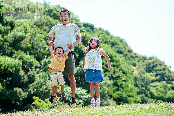 Ein Mann und zwei Kinder springen auf das Gras