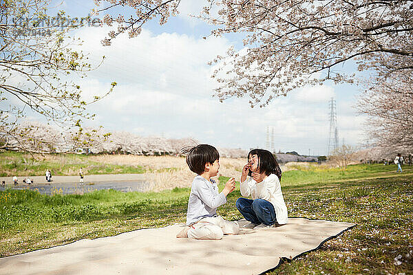 Zwei Kinder sitzen auf einer Decke im Park