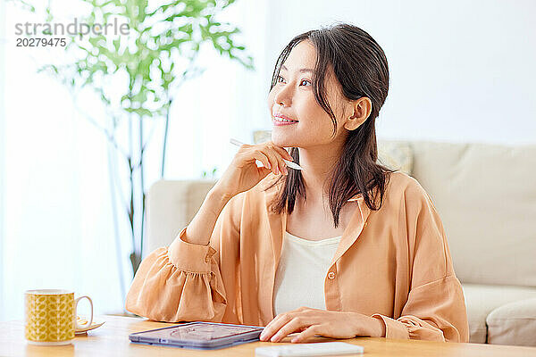 Asiatische Frau sitzt mit Laptop und Kaffee am Tisch