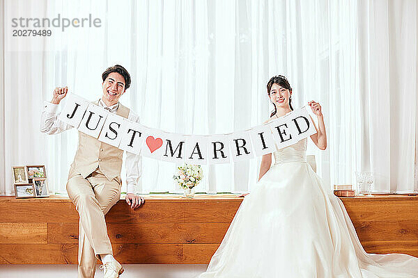 Ein frisch verheiratetes Paar hält ein Banner mit der Aufschrift „Frisch verheiratet“.