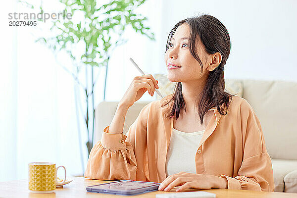 Asiatische Frau sitzt am Tisch mit einem Stift in der Hand