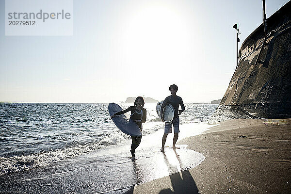 Ein Mann und eine Frau gehen mit Surfbrettern am Strand spazieren