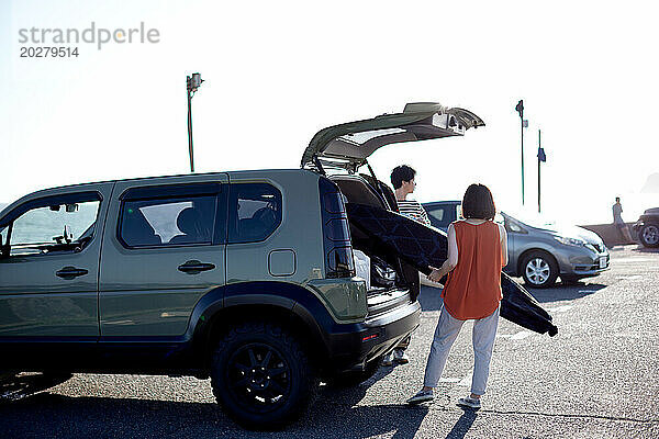 Eine Frau und ein Mann laden ein Surfbrett in den Kofferraum eines Autos