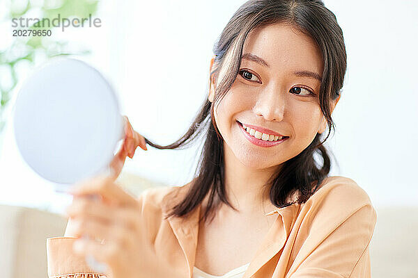 Asiatische Frau lächelt  während sie einen Spiegel hält