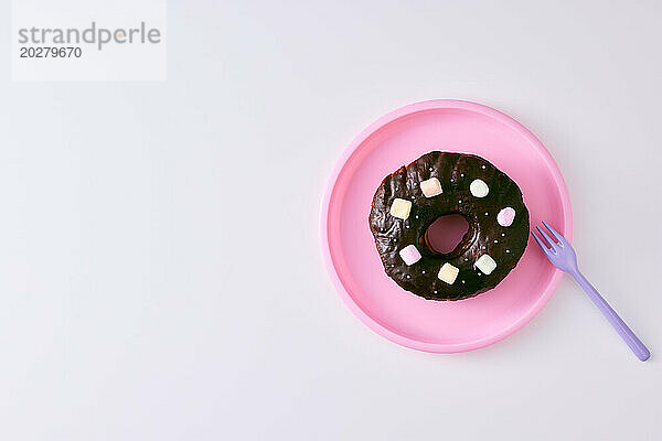 Ein Schokoladendonut mit Marshmallows auf einem rosa Teller