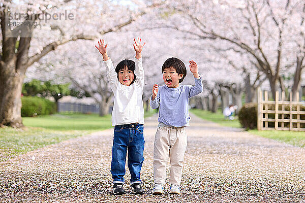 Zwei kleine Jungen stehen mit erhobenen Händen vor einem Baum
