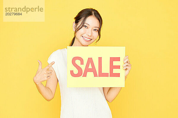 Asiatische Frau hält ein Verkaufsschild auf gelbem Hintergrund hoch