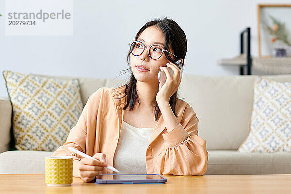 Eine Frau mit Brille sitzt mit einer Tasse Kaffee und einem Tablet an einem Tisch