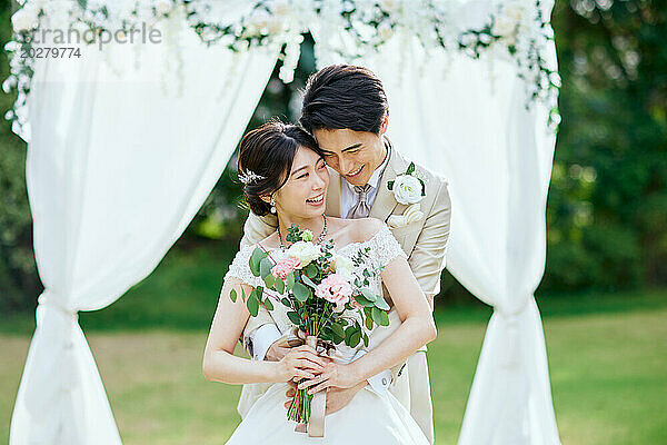 Ein frisch vermähltes Paar umarmt sich unter einem weißen Hochzeitsbogen