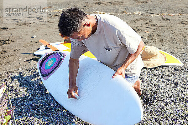 Ein Mann sitzt mit einem Surfbrett am Strand